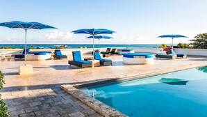Un área junto a la piscina con sillas de descanso y sombrillas, con vista despejada al océano y una piscina.
