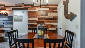 A dining area with a wooden table and chairs, a lantern, and a wall with a rustic wooden panel design. - Abi's Place, No Stairs! Central Location!  Stylish!  3 BDRM 2 BA, Pool Available (Branson)
