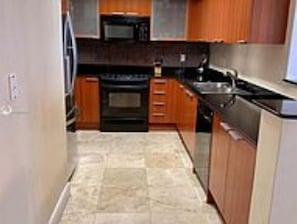 A compact kitchen with wooden cabinets, a black stove, and a stainless steel sink.