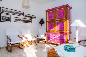 Um quarto com uma cadeira de balanço de madeira, um armário rosa e quadros nas paredes.