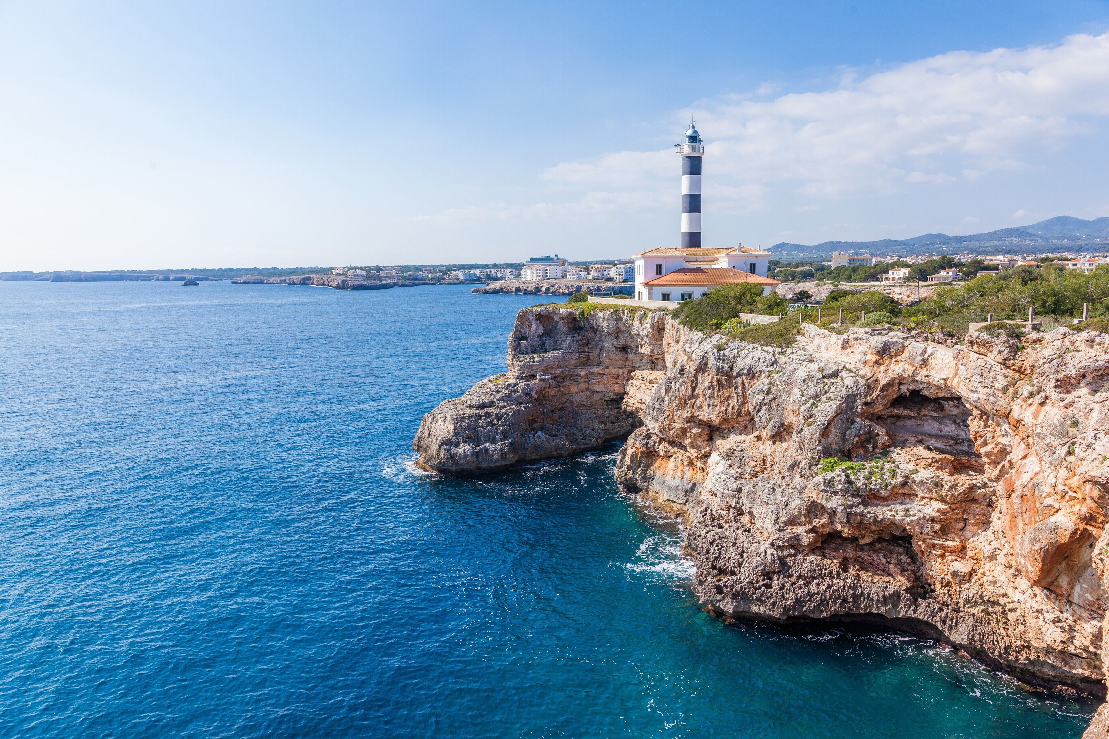 Vista costera con un faro, acantilados rocosos y un mar azul y despejado.