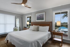 Une chambre avec un grand lit, un ventilateur de plafond et une vue sur une piscine, visible par la fenêtre.