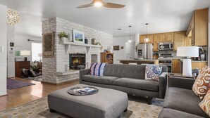 A modern living room with a fireplace, grey sofas, and a dining area with wooden cabinets. - Landhaus Eichenbaum | Pool | Hot Tub (Fredericksburg)