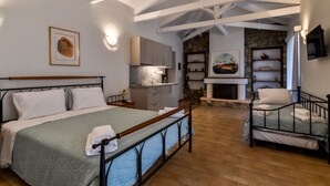 Een slaapkamer met een groot bed, een kleiner bed, een open haard, een keukenhoek en een stenen muur.
