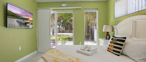 A bedroom with a bed, a ceiling fan, a window, and a wall-mounted TV.