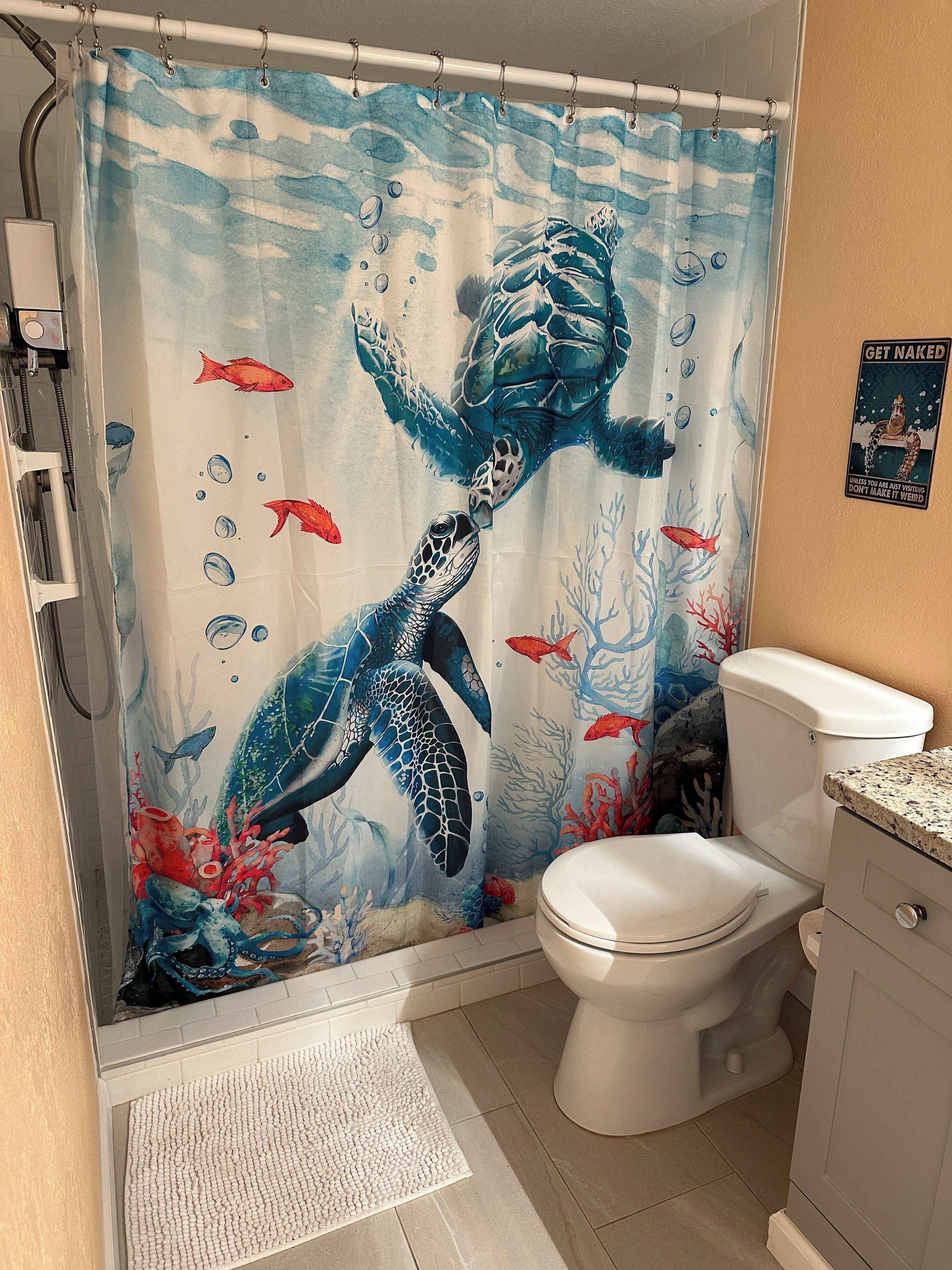 Un baño con cortina de ducha que muestra una tortuga marina y peces, un inodoro y un lavabo.
