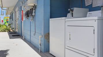 Une buanderie équipée d’un lave-linge Whirlpool blanc, d’un enrouleur de tuyau d’incendie et d’un mur bleu orné d’une fresque.