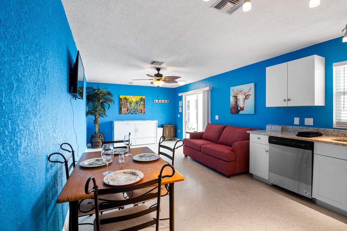 A compact living space with a dining area, a kitchen, and a red sofa.