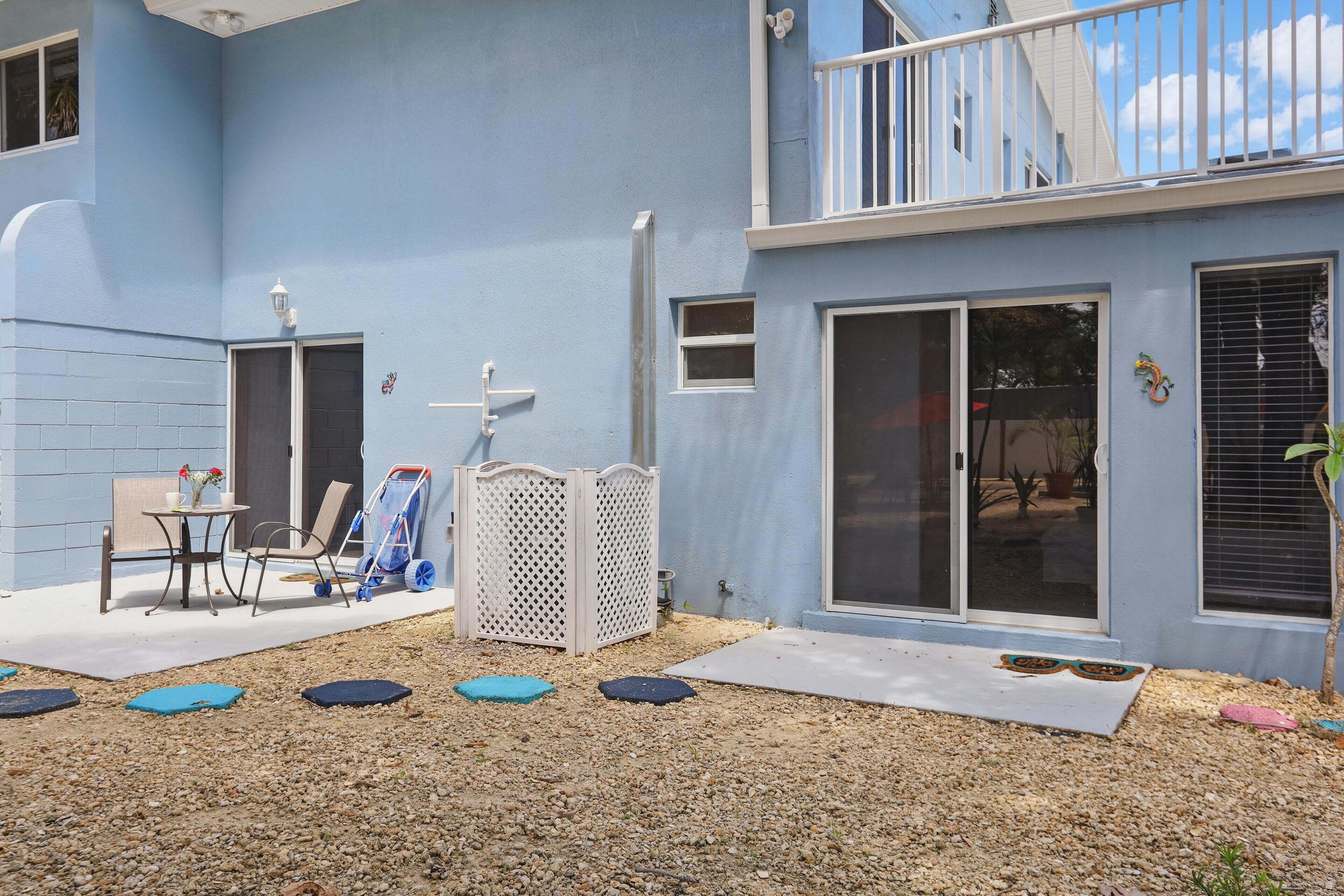Edificio azul con balcón, puerta corredera de vidrio y un pequeño patio con mesa y sillas.