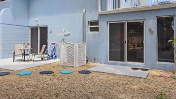 Edificio azul con balcón, puerta corredera de vidrio y un pequeño patio con mesa y sillas.