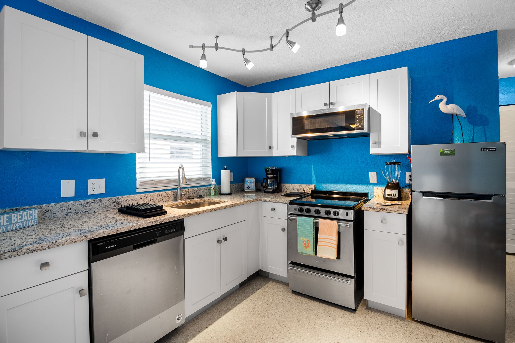 A modern kitchen with white cabinets, a stainless steel refrigerator, and a blue accent wall.