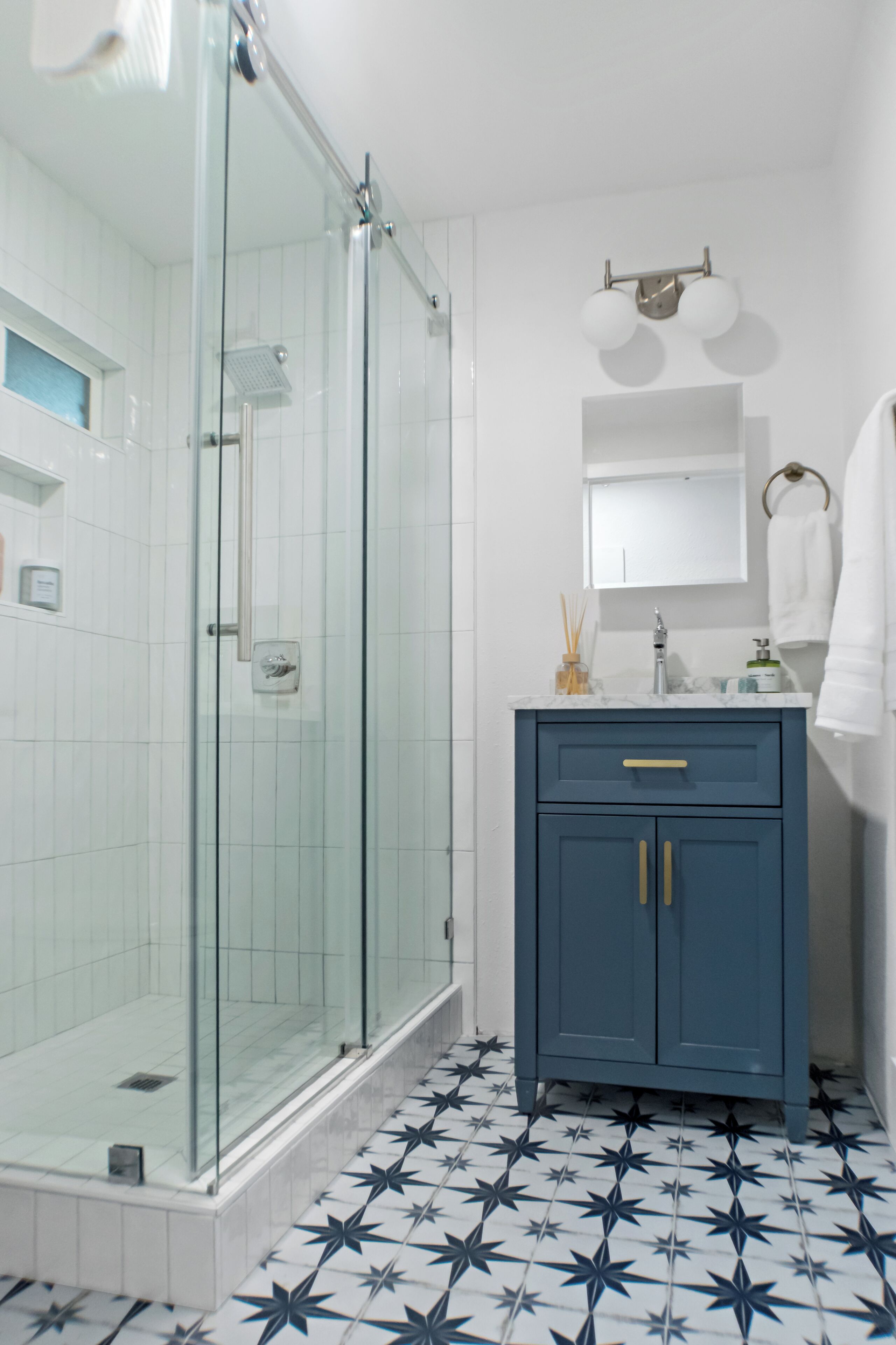 A bathroom with a glass-enclosed shower, a blue vanity with gold handles, and a tiled floor with a star pattern.
