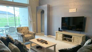 Un salon avec une grande télévision, un fauteuil à motifs et une table basse.
