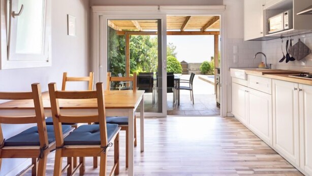 A modern kitchen with wooden cabinets, a dining area with a table and chairs, and a view of the outdoors through a glass door. - Vacation home Jorge by Interhome (El Rosario)
