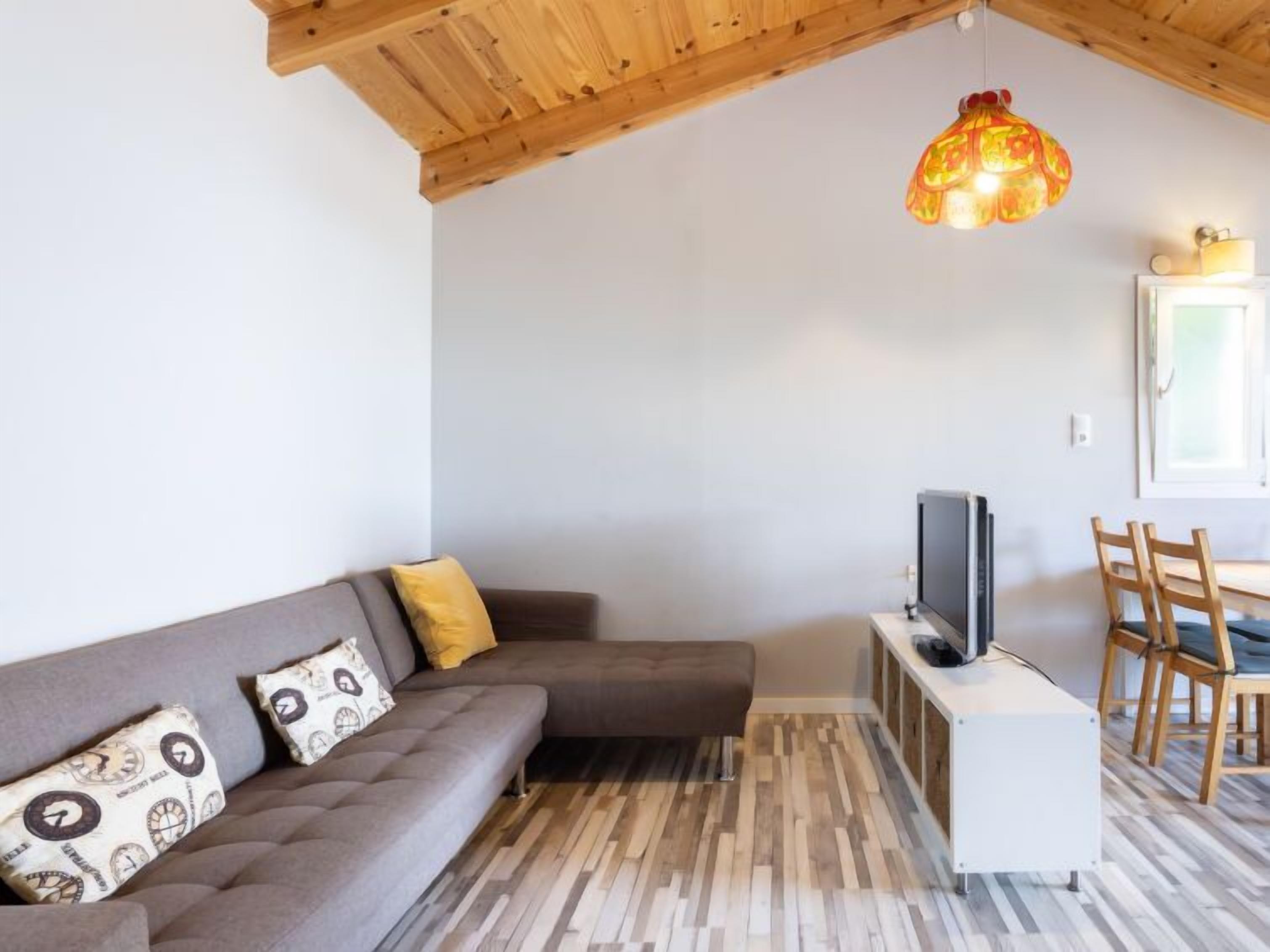 Una sala de estar con un sofá, un televisor sobre un mueble bajo, techo de madera y una lámpara colgante.