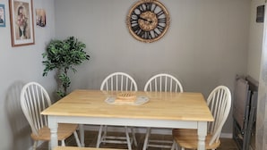Ein Esszimmer mit Holztisch, einer Bank, weißen Stühlen, einer dekorativen Wanduhr und gerahmten Bildern.