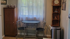 Ein kleiner Essbereich mit Tisch, Stühlen, einem Holzschrank, einer Uhr und einem Mülleimer.