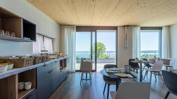 Una cucina moderna con soffitto in legno, una zona pranzo con vista sul mare e un balcone con tavolo e sedie.