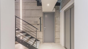 Un intérieur moderne avec un escalier menant au premier étage, une porte fermée et un luminaire fixé au mur.