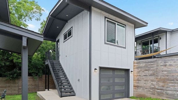 Une maison moderne à deux étages, dotée d’un garage, d’un escalier et d’un espace extérieur couvert.