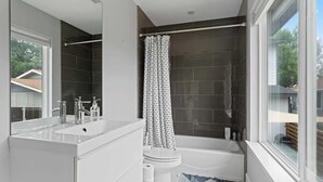 Une salle de bain moderne avec un grand miroir, un lavabo blanc, une baignoire et un rideau de douche.