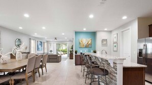A spacious kitchen with a central island, a dining area with a wooden table and chairs, and a living area with a sofa and a coffee table. - Cheery Villa with Games Room at Encore (Kissimmee)
