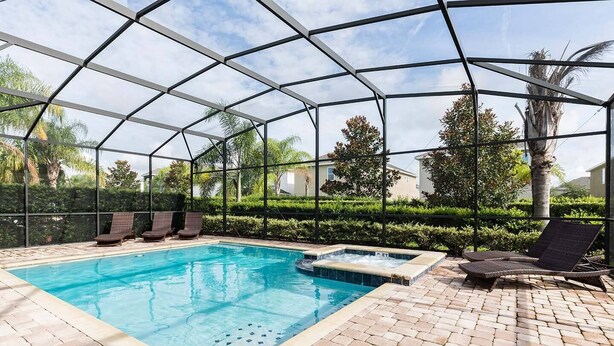 A covered swimming pool with lounge chairs and a hot tub, surrounded by greenery and a clear sky. - Cheery Villa with Games Room at Encore (Kissimmee)