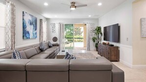 A modern living room with a sectional sofa, a flat-screen TV, and a ceiling fan. - Cheery Villa with Games Room at Encore (Kissimmee)