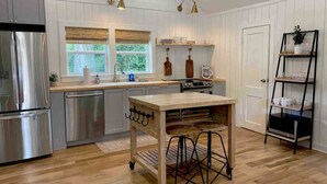 A modern kitchen with wooden cabinets, a stainless steel refrigerator, a wooden island with stools, and pendant lighting. - The Belmont Cottage - 2 bedroom (Belmont)