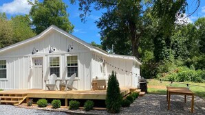 A white building with a wooden deck, outdoor seating, and a small tree. - The Belmont Cottage - 2 bedroom (Belmont)