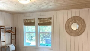 A bedroom with a bed, a wooden headboard, a window with a view, a wall-mounted mirror, and a ceiling light. - The Belmont Cottage - 2 bedroom (Belmont)