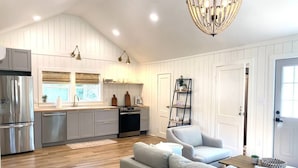 A spacious kitchen with modern appliances, a dining area with a grey sofa, and a chandelier. - The Belmont Cottage - 2 bedroom (Belmont)