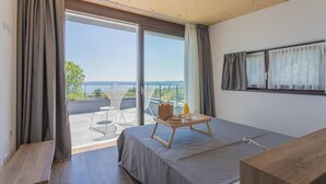 Un dormitorio moderno con una cama grande, una mesita de noche de madera y un balcón con vistas al mar.