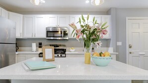 Een moderne keuken met witte kasten, roestvrijstalen apparatuur en een centraal eiland met een bloevas en een fruitschaal.