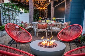 Une terrasse extérieure avec un foyer rond, des chaises en osier et une table dressée pour le repas.