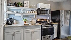 Een moderne keuken met witte kastjes, een roestvrijstalen koelkast, een magnetron, een gasfornuis en een spoelbak.