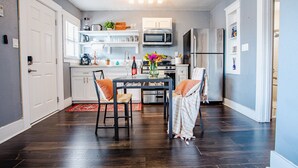 Een moderne keuken met donker houten vloeren, witte kasten, een roestvrijstalen koelkast en een eethoek met een tafel en stoelen.