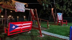 A swing set with a flag, a sign, and string lights in a backyard. - 2BR Beach Escape in Luquillo • Walk to Beach • Near Kiosks (luquillo)