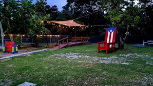 A backyard with a wooden deck, string lights, and a red and white chair. - 2BR Beach Escape in Luquillo • Walk to Beach • Near Kiosks (luquillo)