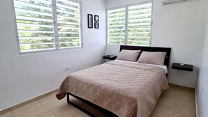 A bedroom with a bed, two nightstands, a window with blinds, and a wall-mounted shelf. - 2BR Beach Escape in Luquillo • Walk to Beach • Near Kiosks (luquillo)