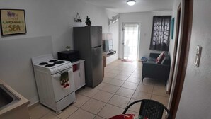 A compact kitchen with a stove, refrigerator, and microwave. A small dining area is visible with a chair and a table. - 2BR Beach Escape in Luquillo • Walk to Beach • Near Kiosks (luquillo)