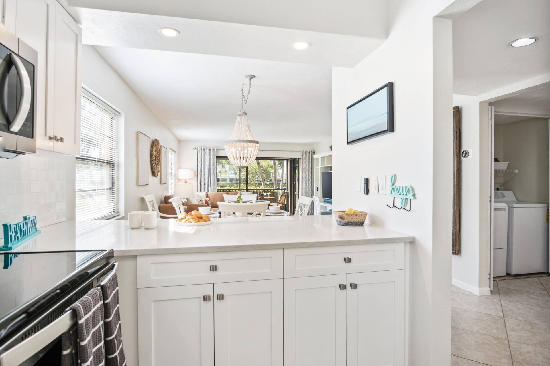 A modern kitchen with white cabinetry, a large island, and a dining area with a chandelier.