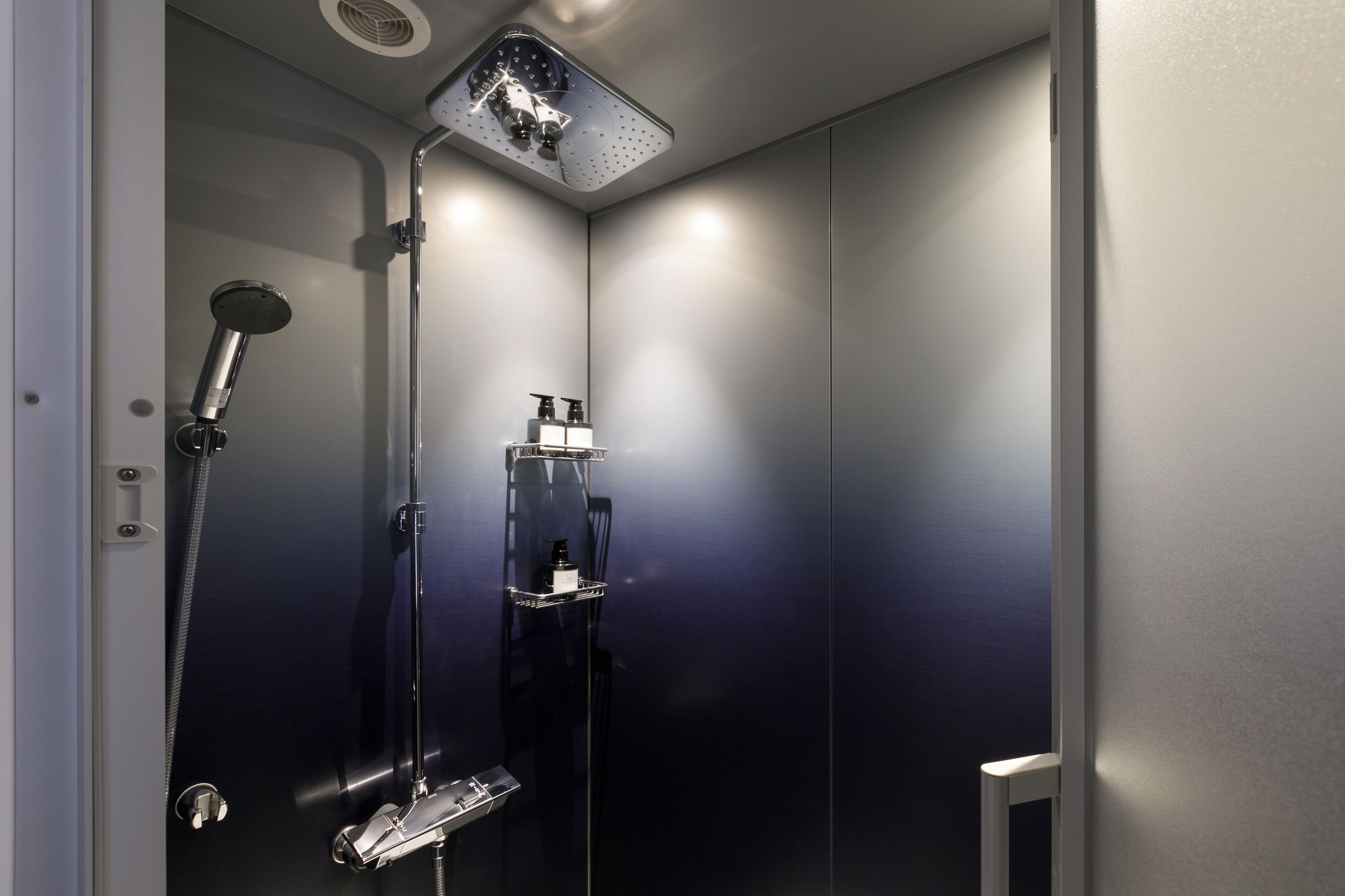 Une douche moderne équipée d’un pommeau de douche à main, d’un robinet mural et d’une étagère pour les articles de toilette.