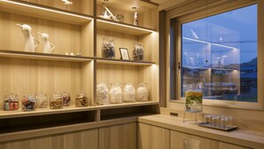 Une cuisine moderne avec des étagères en bois où sont exposés des bocaux contenant des aliments, et une grande fenêtre donnant sur l’extérieur.