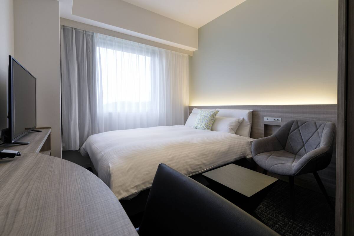 A hotel room with a bed, a chair, a TV, and a desk.