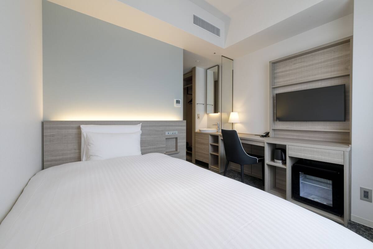 A hotel room with a bed, a desk, a chair, a TV, and a fireplace.