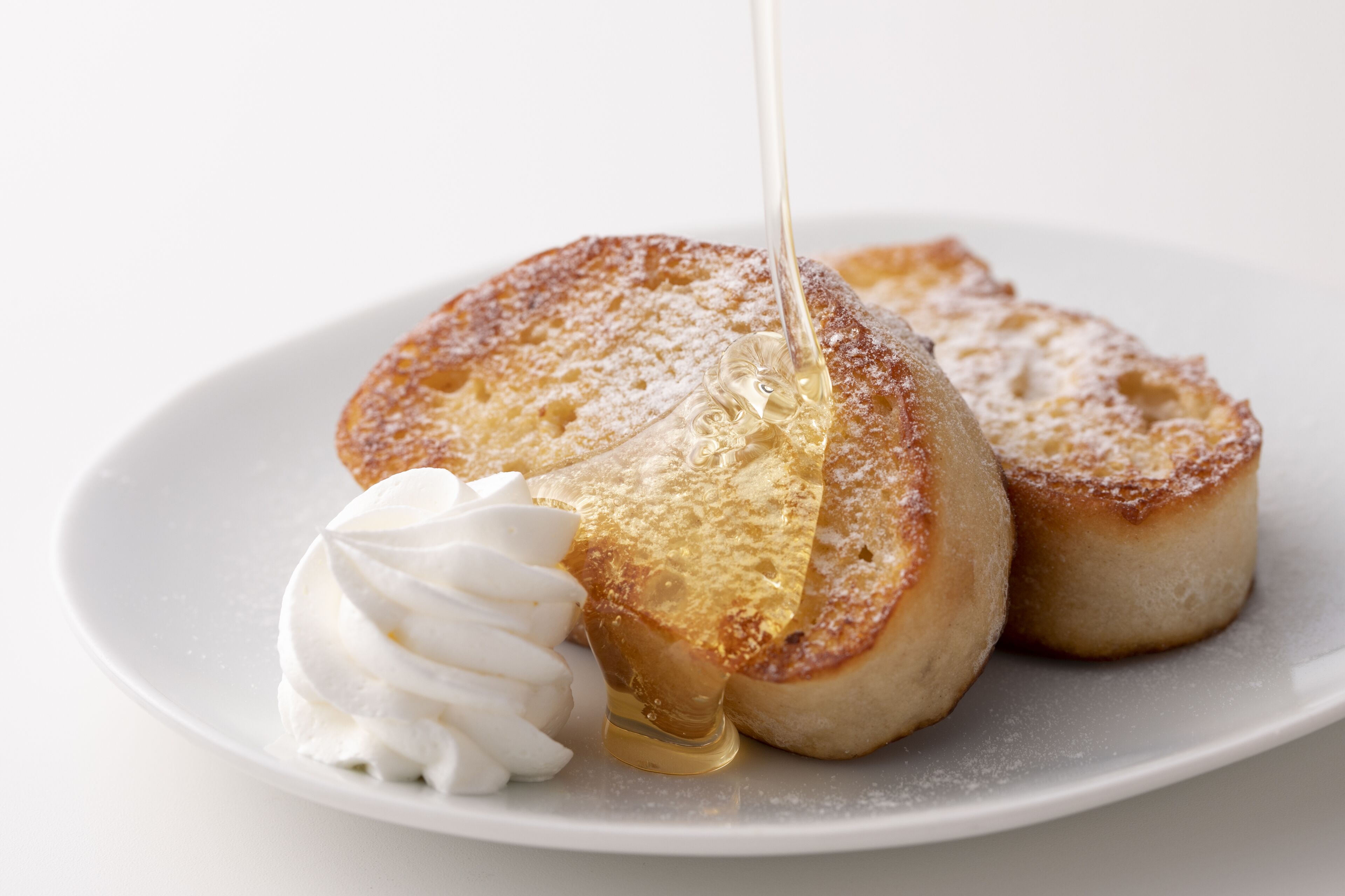 A plate with two pieces of toast and a dollop of whipped cream, with syrup being poured over the toast.