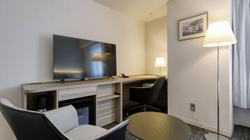 Ein Hotelzimmer mit Flachbildfernseher, Schreibtisch, Stuhl, Lampe und kleinem Tisch.