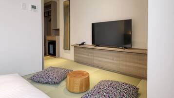 Ett modernt hotellrum med en stor platt-TV som är monterad på ett träskåp, en säng med mönstrade kuddar och en liten träpall.
