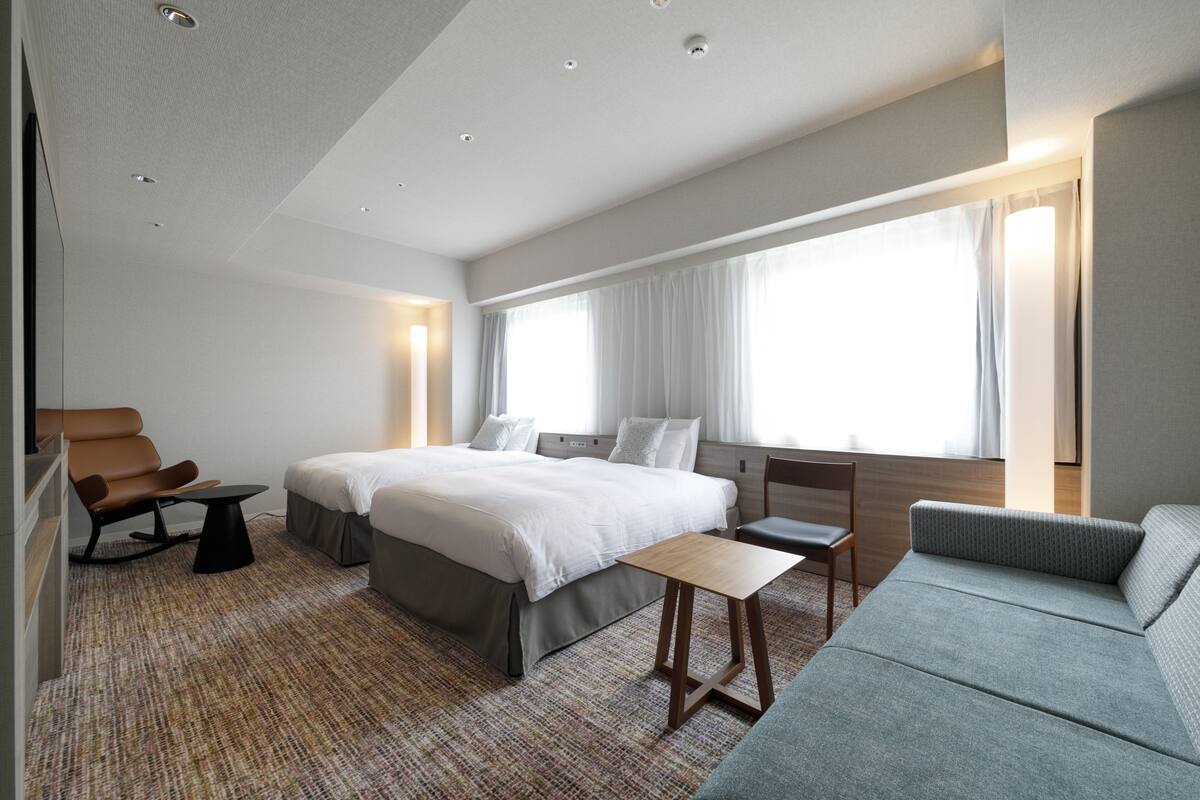A modern hotel room with a large bed, a sofa, a desk, and a chair.